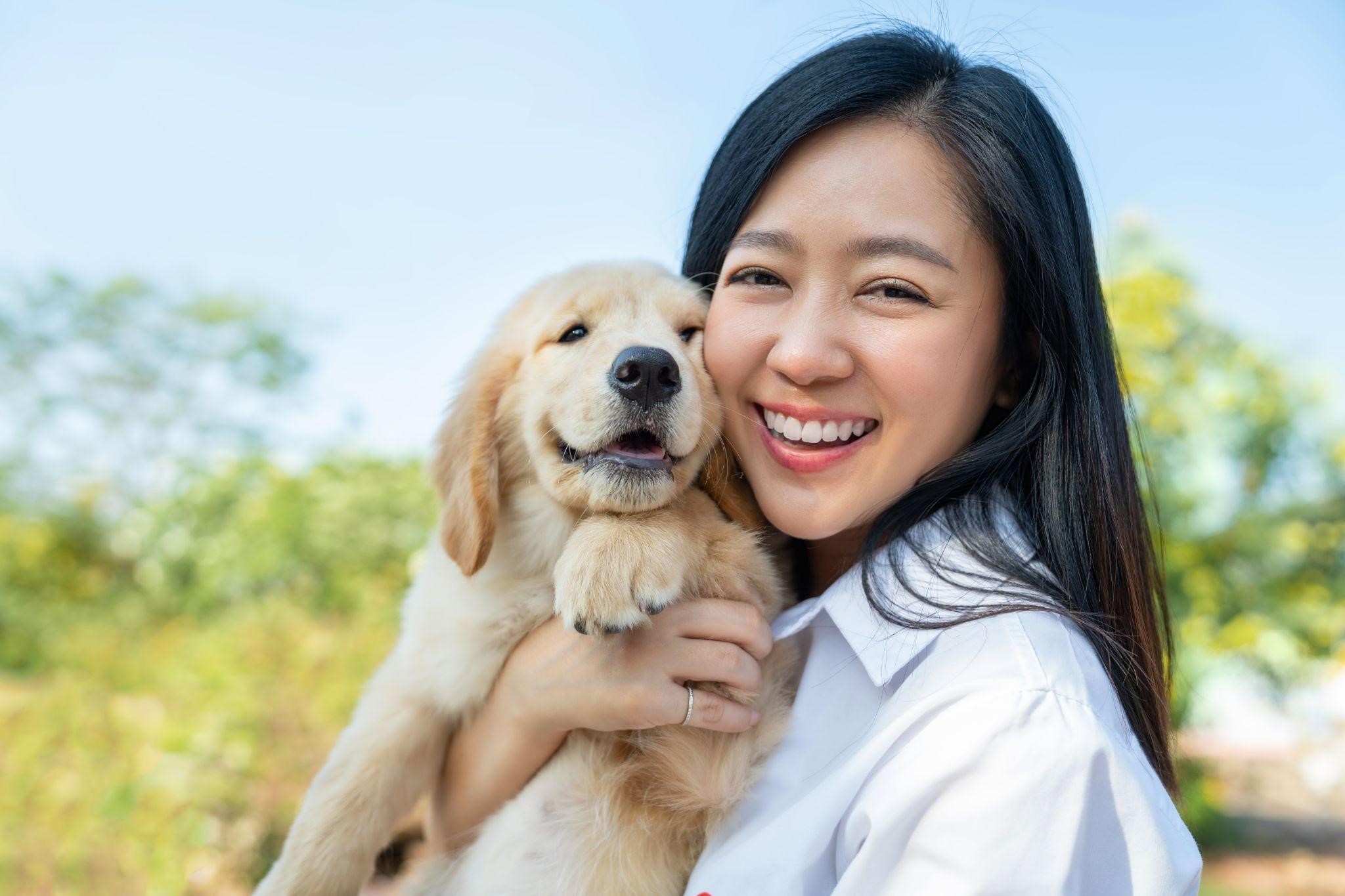 A woman smiling and holding a golden retriever puppy, wondering, “How much is a golden retriever puppy?