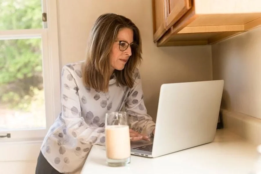 A middle-aged woman working on a laptop, at her kitchen counter.