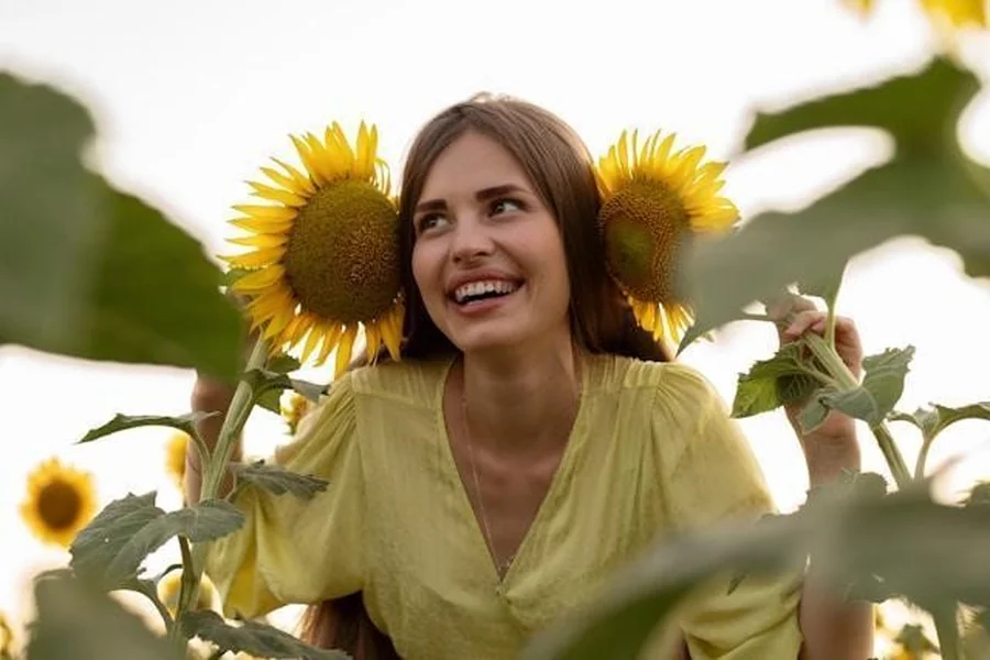 A girl in a yellow dress, smiling in a field of sunflowers.