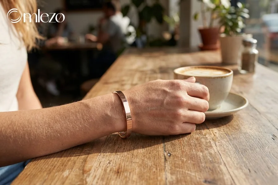 Person wearing an Omlezo rose gold magnetic copper bracelet while enjoying coffee at a cafe table